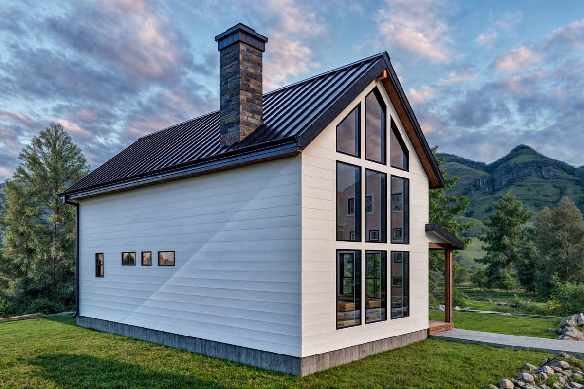 Modern house plan exterior with a dark metal roof, stone chimney, and a large gable window wall.