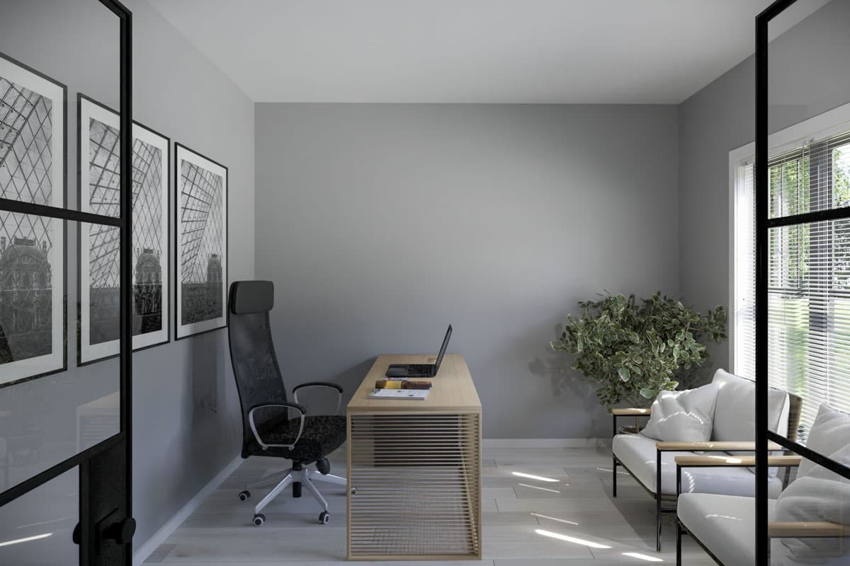 A modern home office with a desk, chair, artwork, and a small seating area. Natural light from a window.