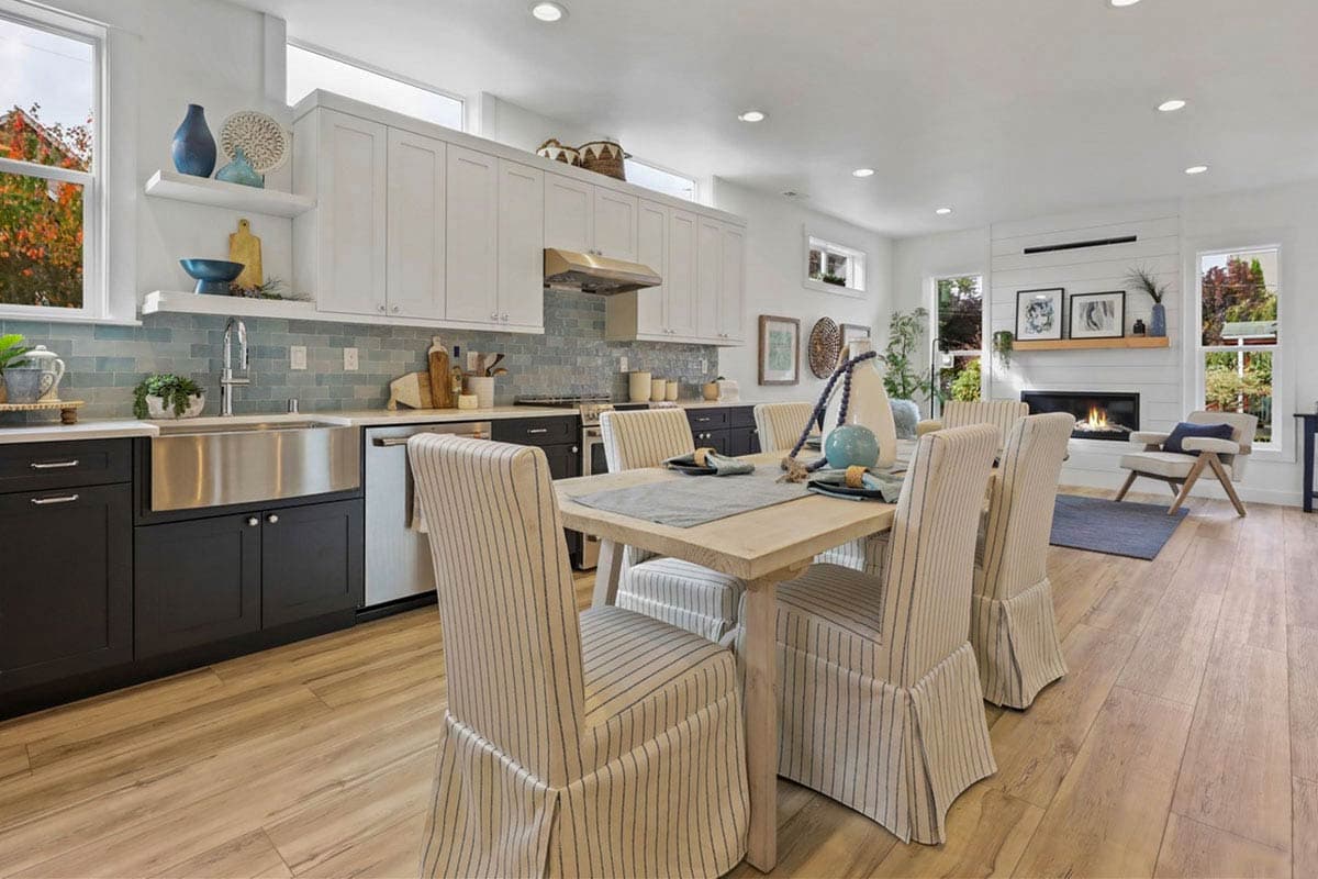 Open concept dining area and kitchen with island, subway tile backsplash, dining table, and fireplace.