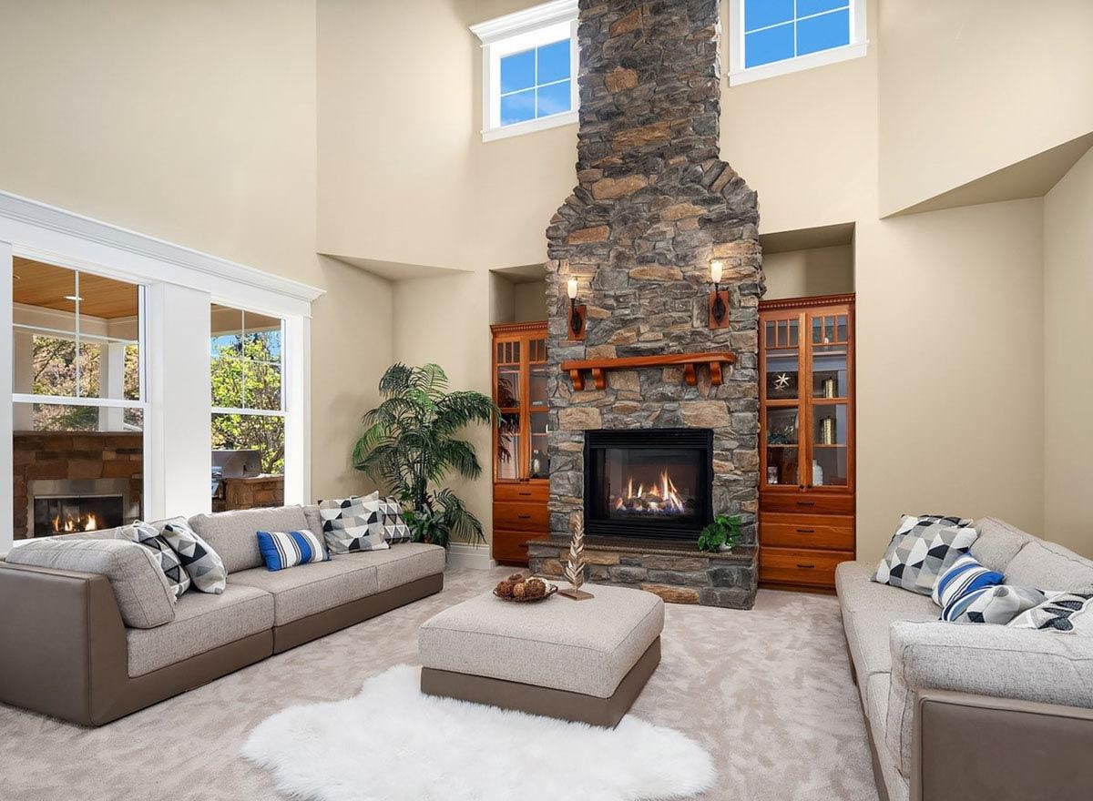 Great room with vaulted ceiling, stone fireplace, built-in cabinetry, and large windows.