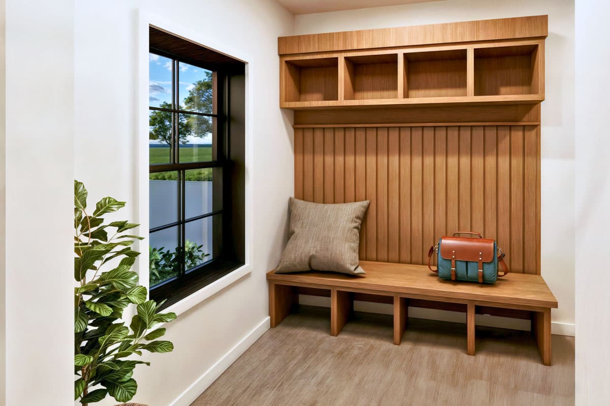 A modern entryway features a wooden bench with a pillow and satchel. Above is a built-in shelf. A window offers a view of trees outside.