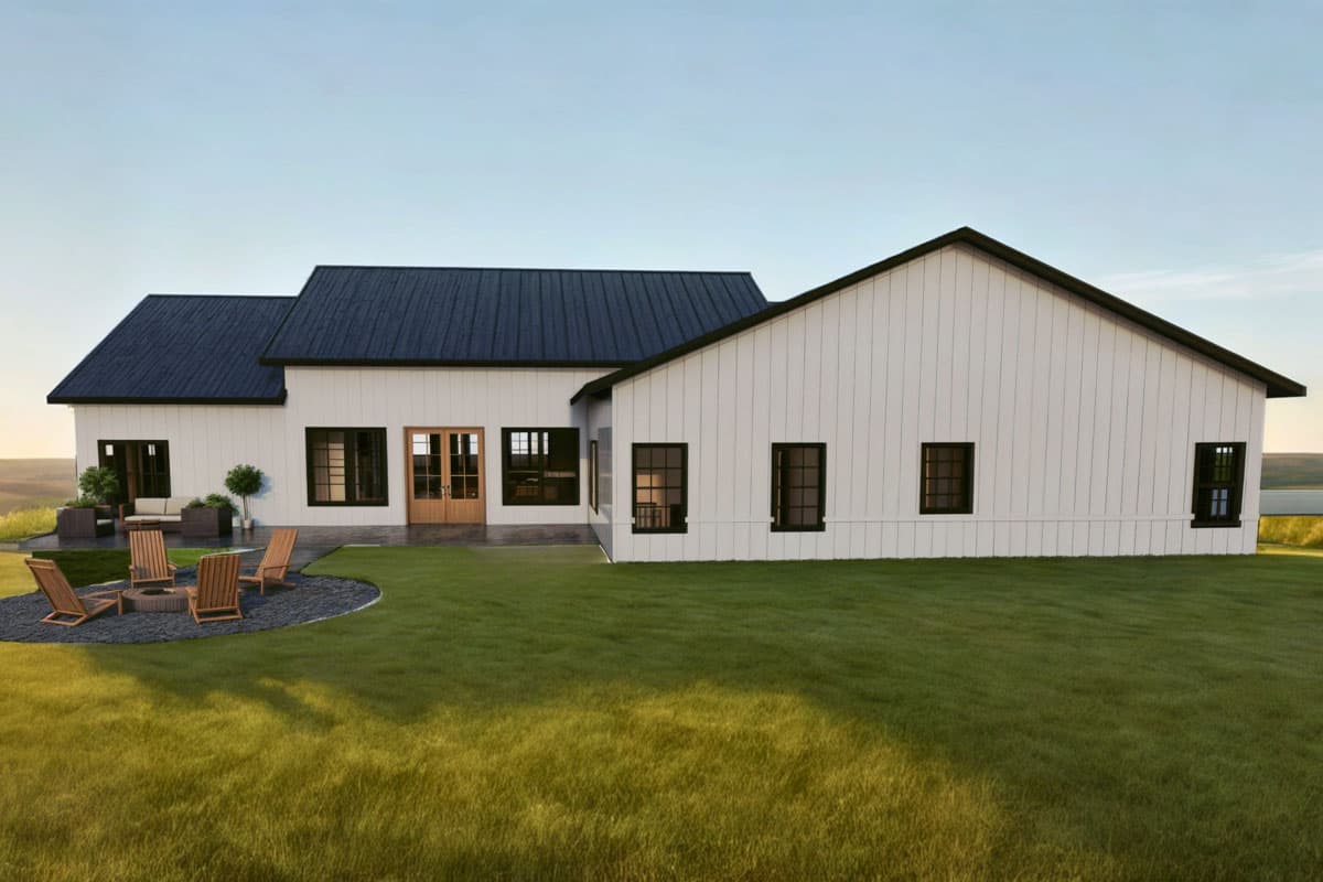 Exterior view of a modern farmhouse with white siding, black roof, and manicured lawn. A fire pit and seating are in the foreground.