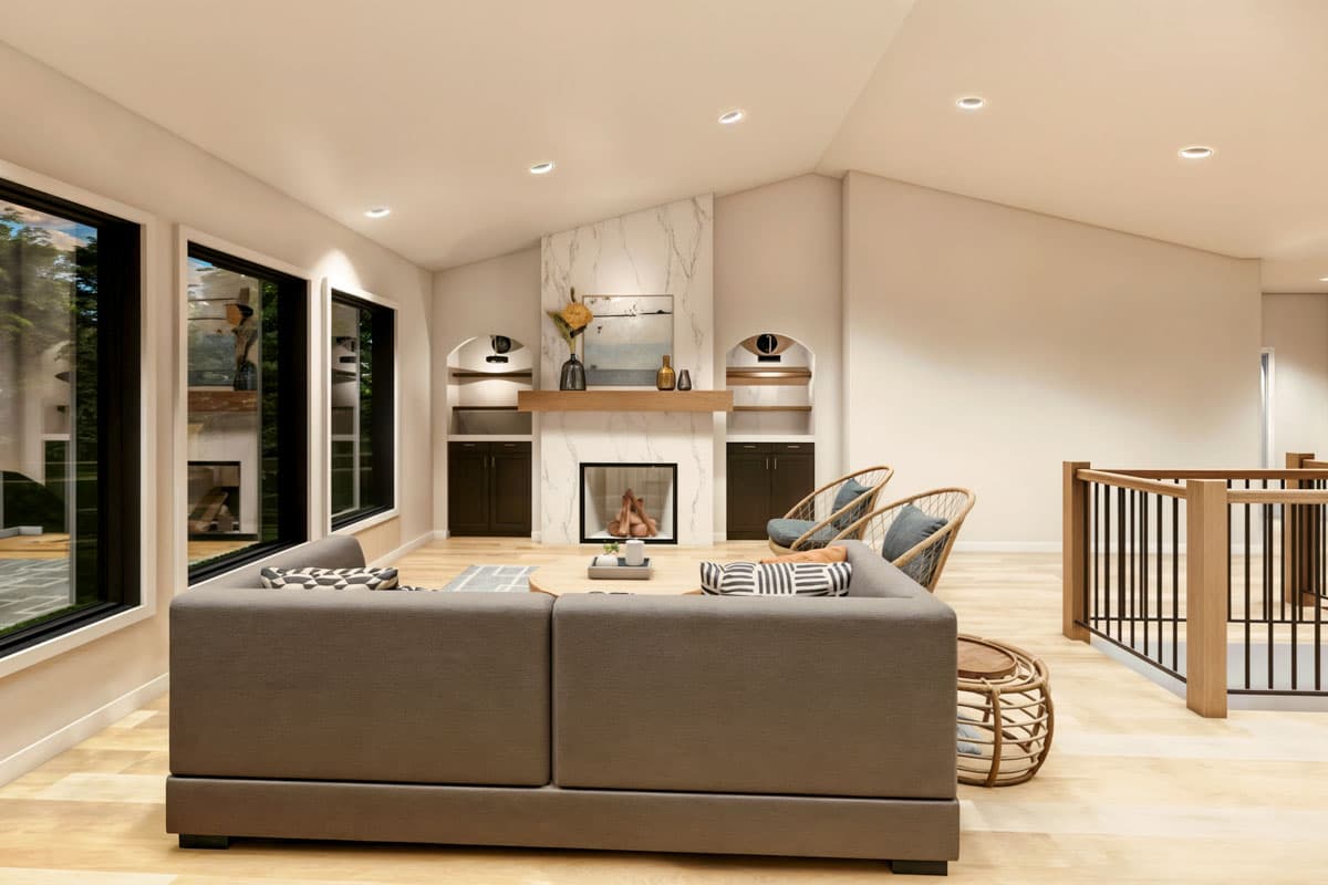 Modern living room featuring a fireplace with marble surround, a large gray sectional sofa, and two wicker chairs. Large windows offer a view.