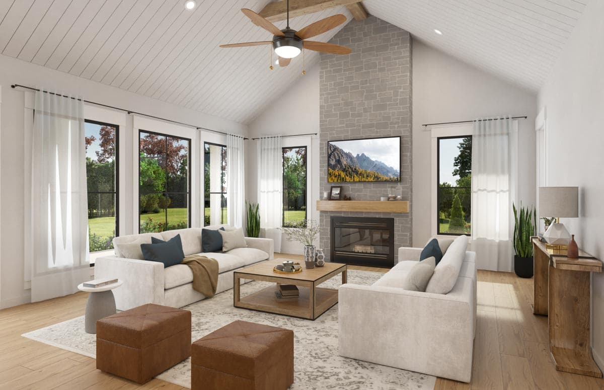 Great room with vaulted beam ceiling, stone fireplace with television, and large windows.