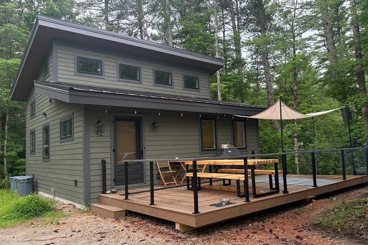Modern two-story house plan with horizontal siding, a prominent gable roof, and a large wrap-around deck.