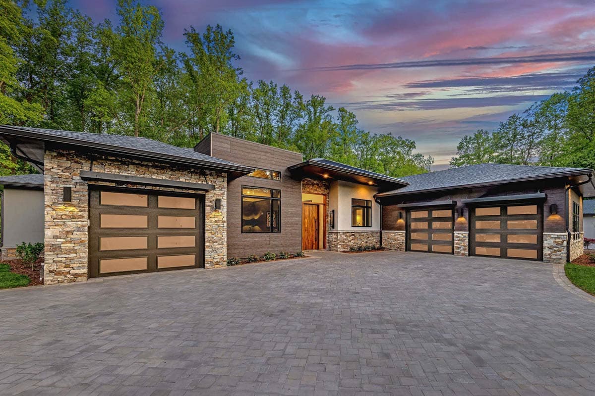 House plan exterior. Modern style, single story. Features include stone accents, flat rooflines, and multiple garage bays with glass panels.