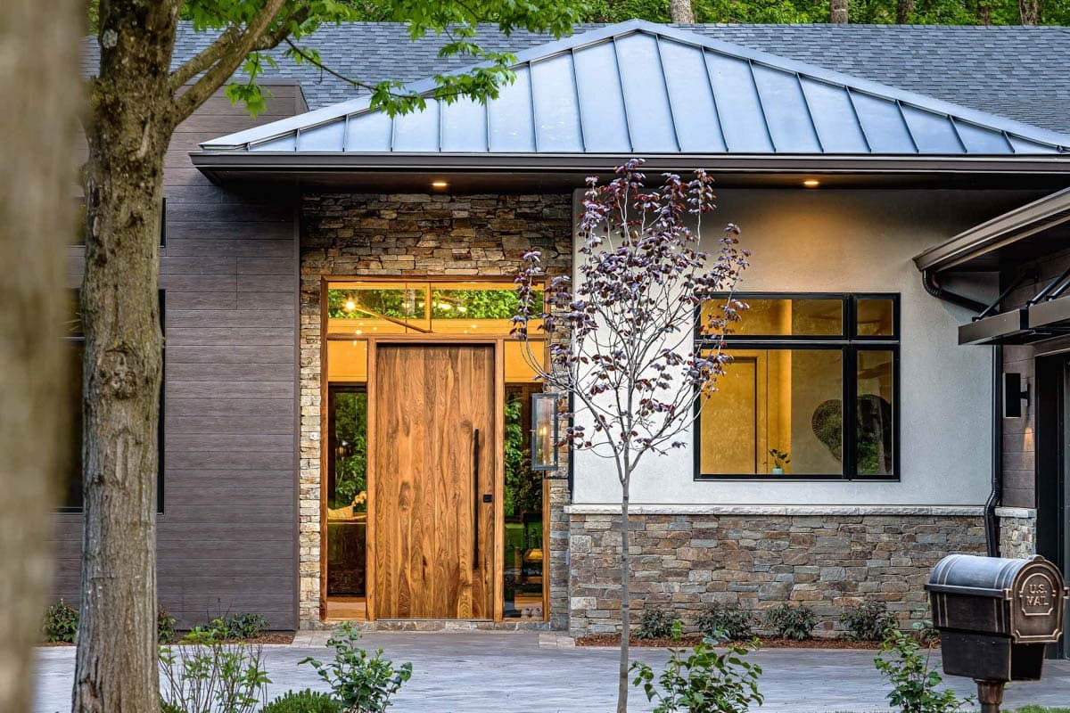 House plan exterior with contemporary style, featuring a metal roof, stone facade, and large wood pivot door.