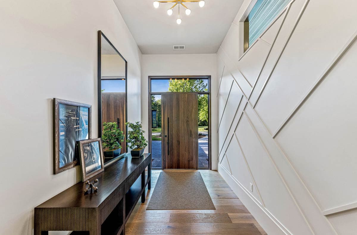 Interior entryway with a tall mirror, console table, modern door with sidelights, and geometric wall paneling.