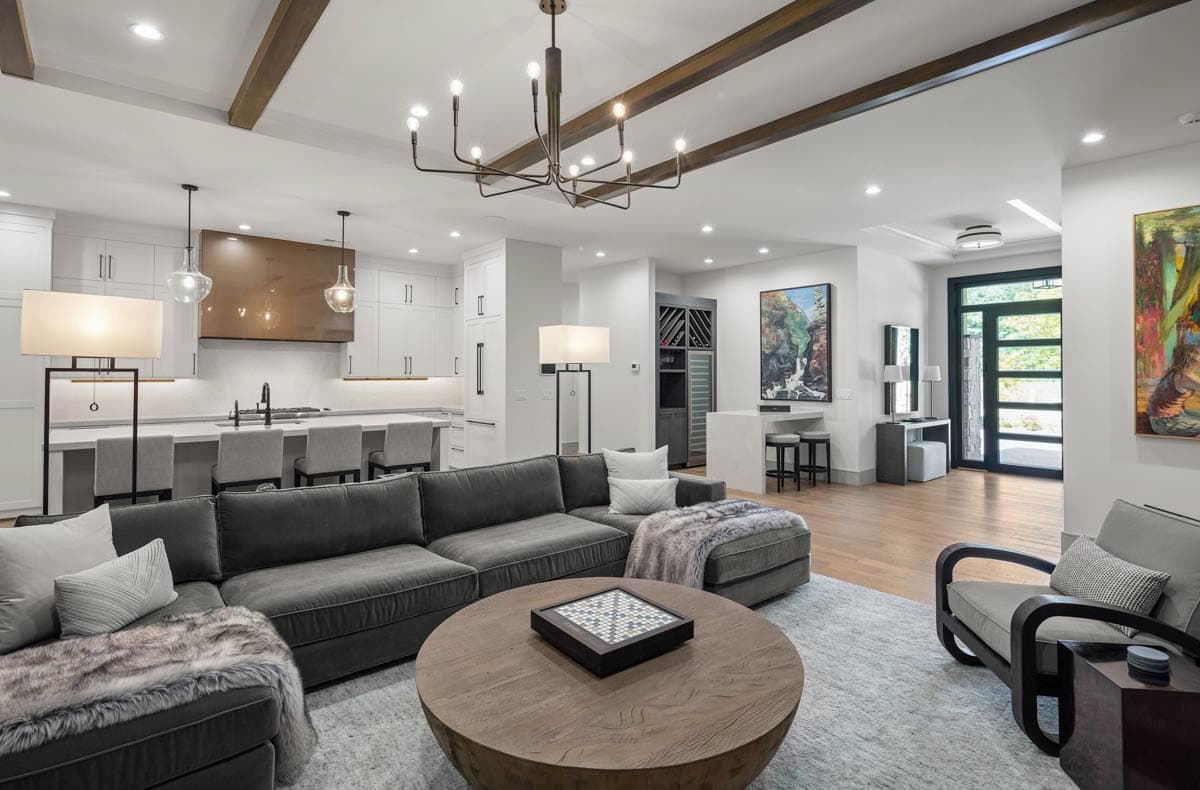 Open concept living area with beamed ceiling, large sectional sofa, kitchen island, and modern fireplace.