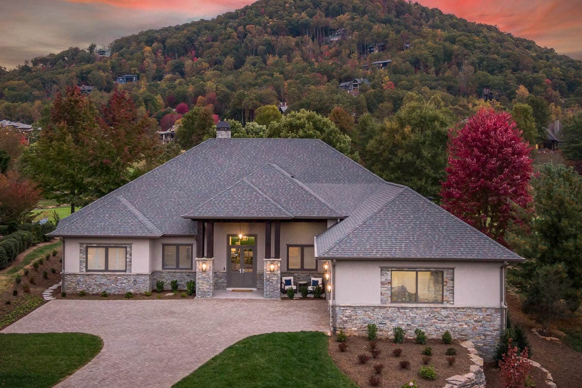 House plan exterior: one-story dwelling with wide eaves, stone accents, pitched rooflines, and a covered entry with columns.