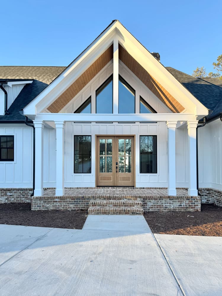 House plan exterior: Modern farmhouse style with a covered porch, prominent gables, vertical siding, and brick foundation.