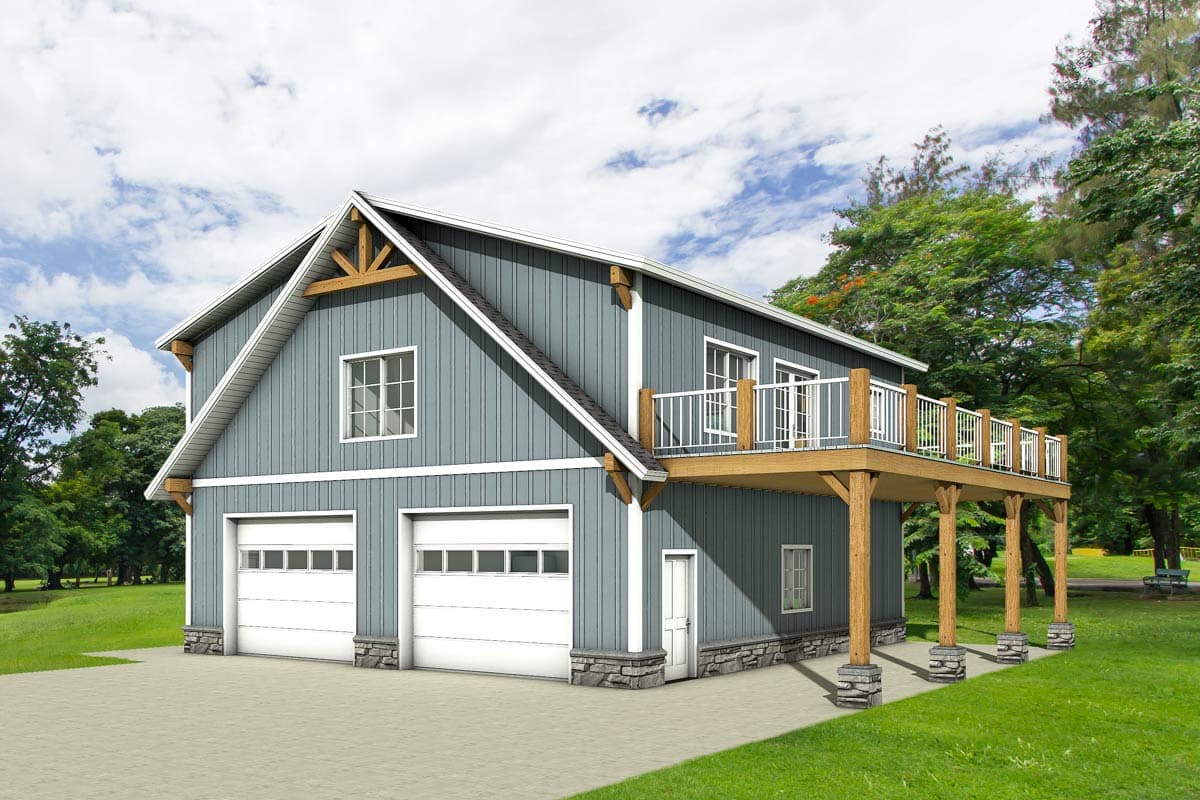A two-story blue-gray building with a second-floor deck and two garage bays sits in front of green trees under a cloudy sky.