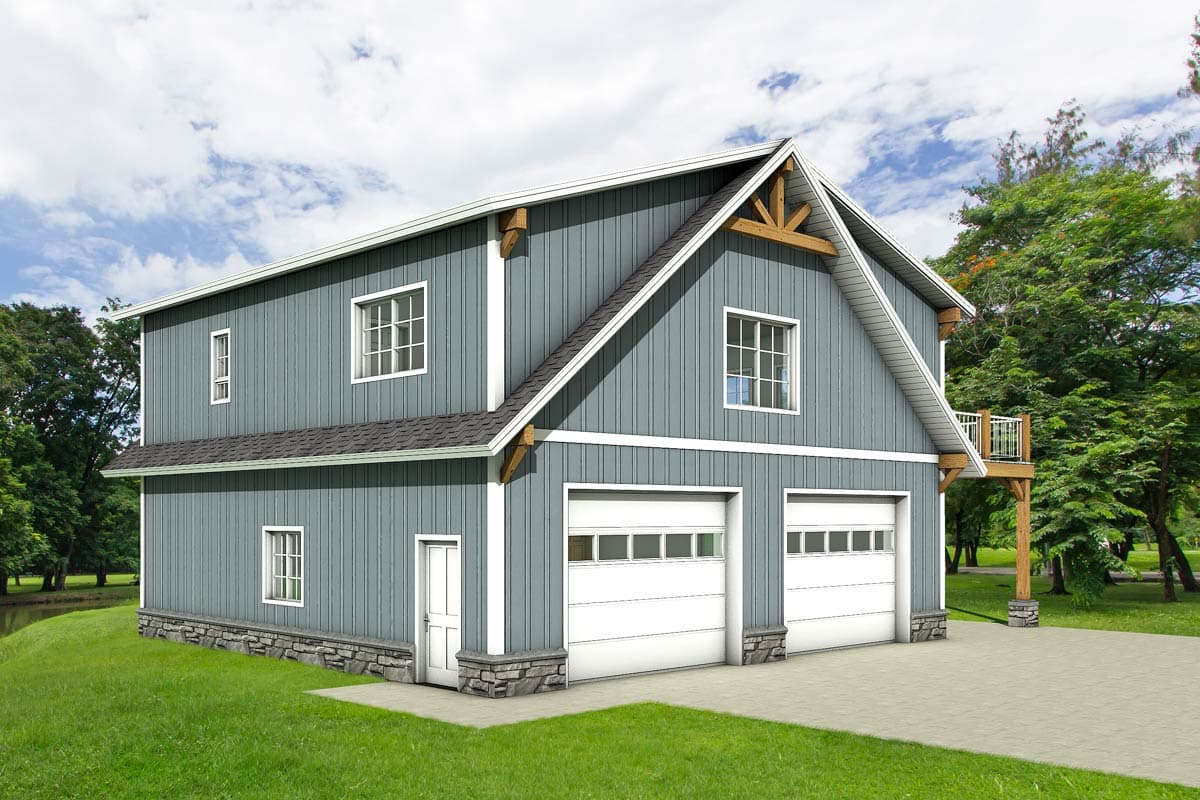 A two-story blue-gray building with white trim, a gabled roof, and two garage doors. A small balcony extends from the side, surrounded by trees.