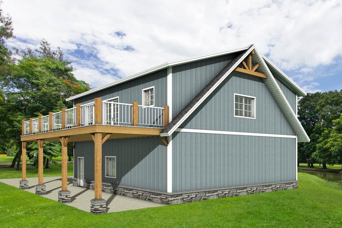 A two-story house with a wraparound deck supported by wooden pillars sits on a grassy area. The house has gray siding and a gabled roof.