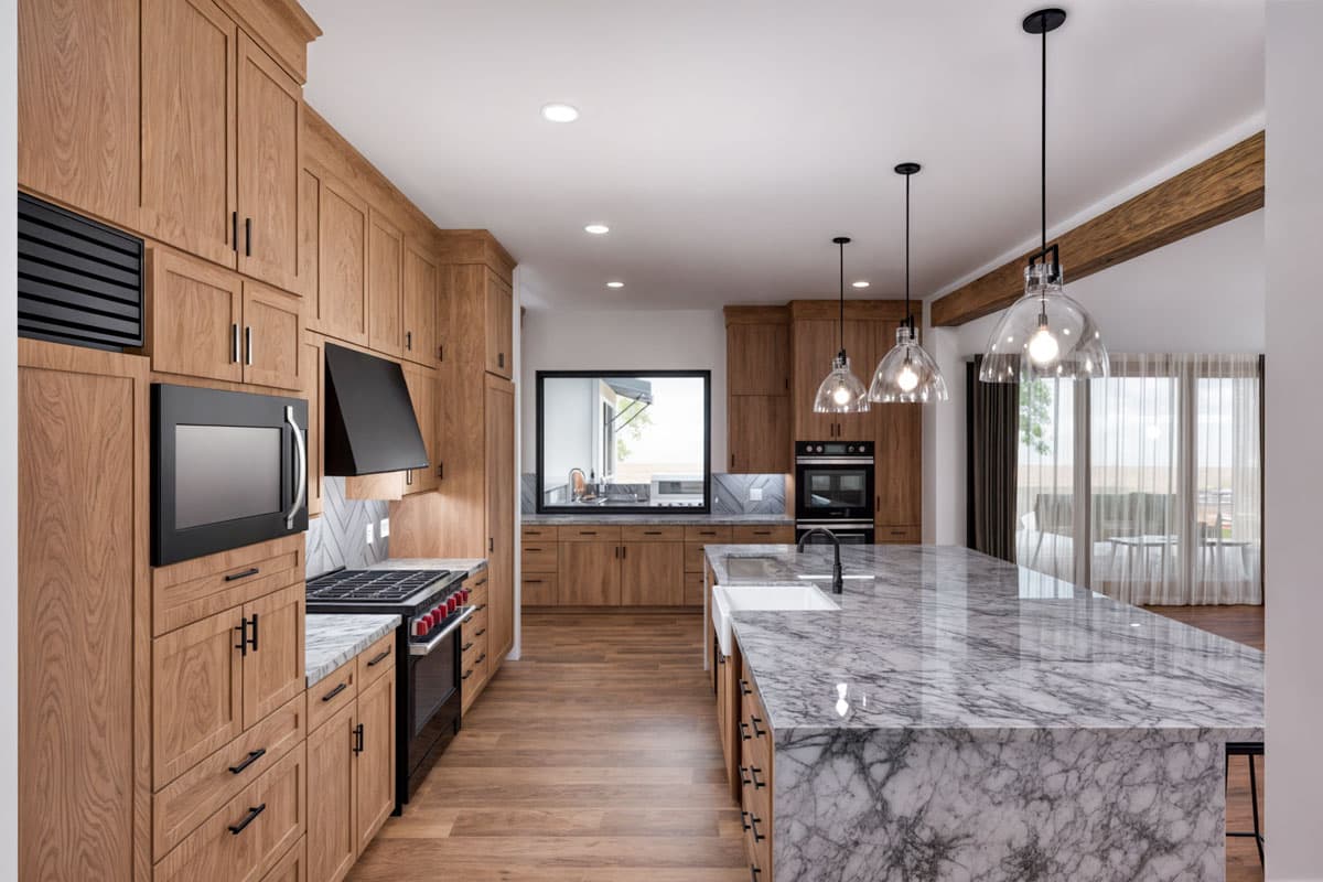 Modern kitchen with wood cabinetry, marble island, stainless steel appliances, and pendant lighting.