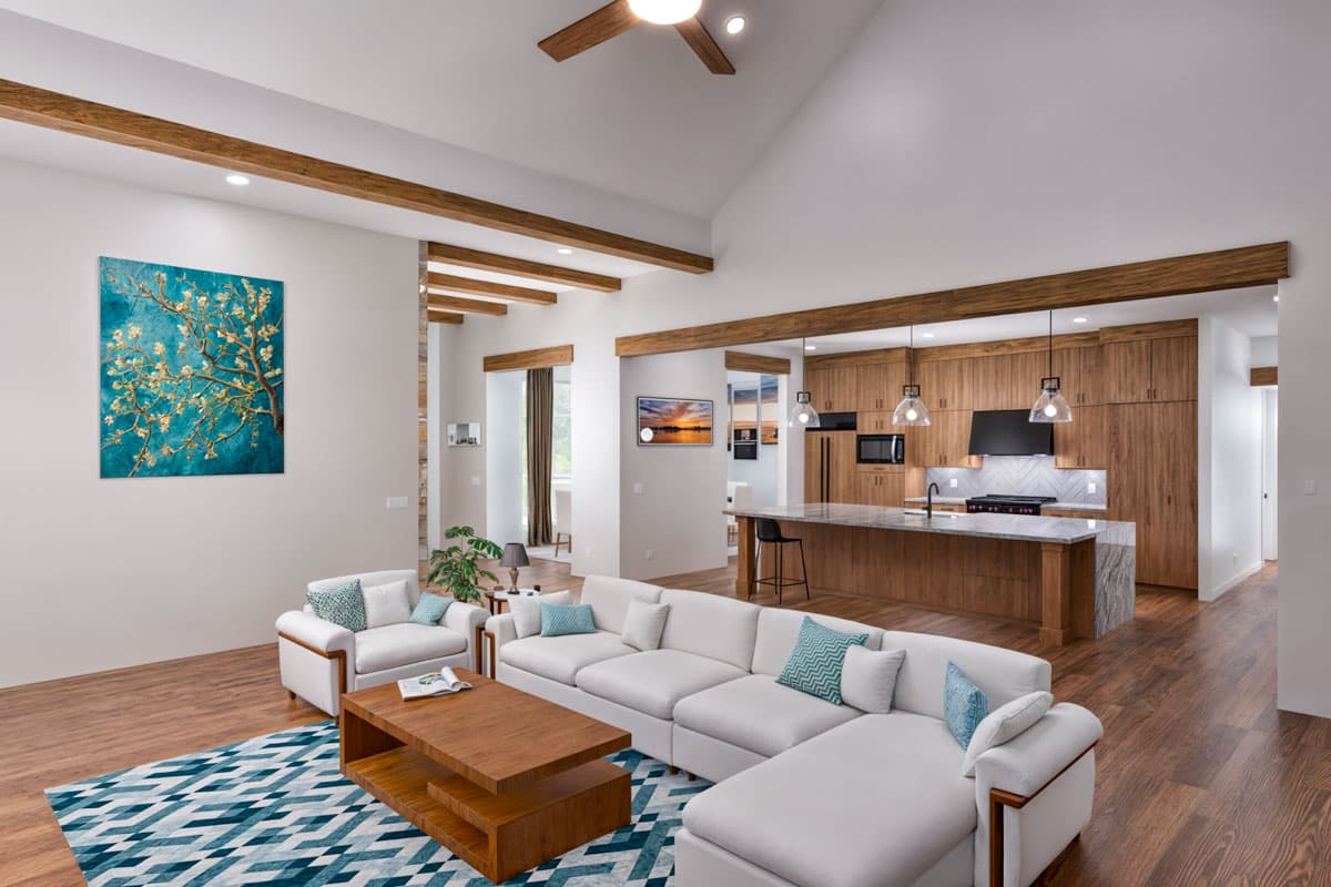 Open concept living and kitchen area with vaulted ceiling, exposed beams, large island with seating, and wood cabinetry.