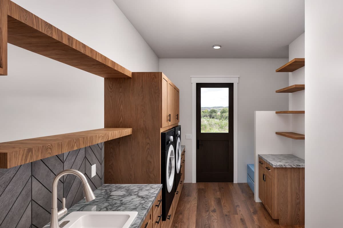 Laundry room interior rendering with stacked washer/dryer, wood cabinetry, stone countertop, sink, open shelving, and exterior door.