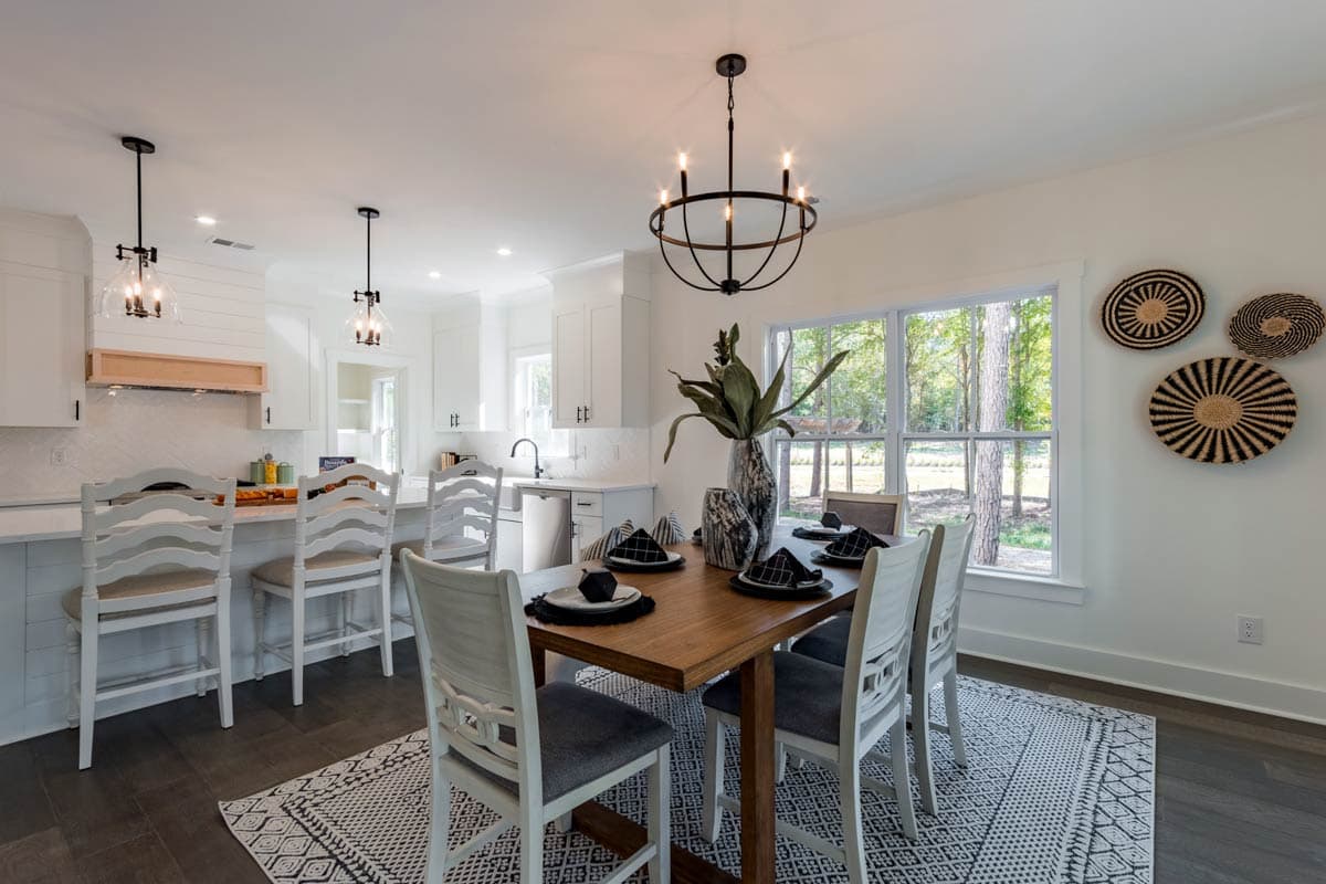 Open-concept dining and kitchen area with island seating, white cabinetry, wood dining table, and large windows.