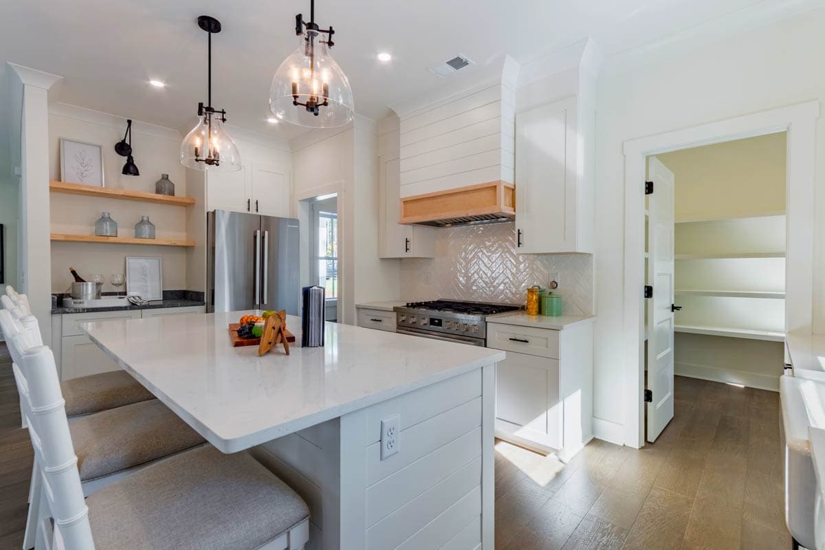 Kitchen with large island, stainless steel range, shiplap range hood, open shelving, and pantry.