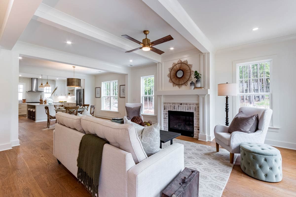 Living room with fireplace, seating area and open view to kitchen. Coffered ceiling, natural light.