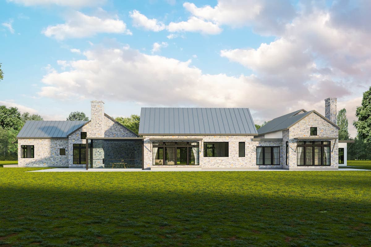 House plan exterior: Modern stone house with metal roof, prominent chimneys, large windows, and covered outdoor seating area.