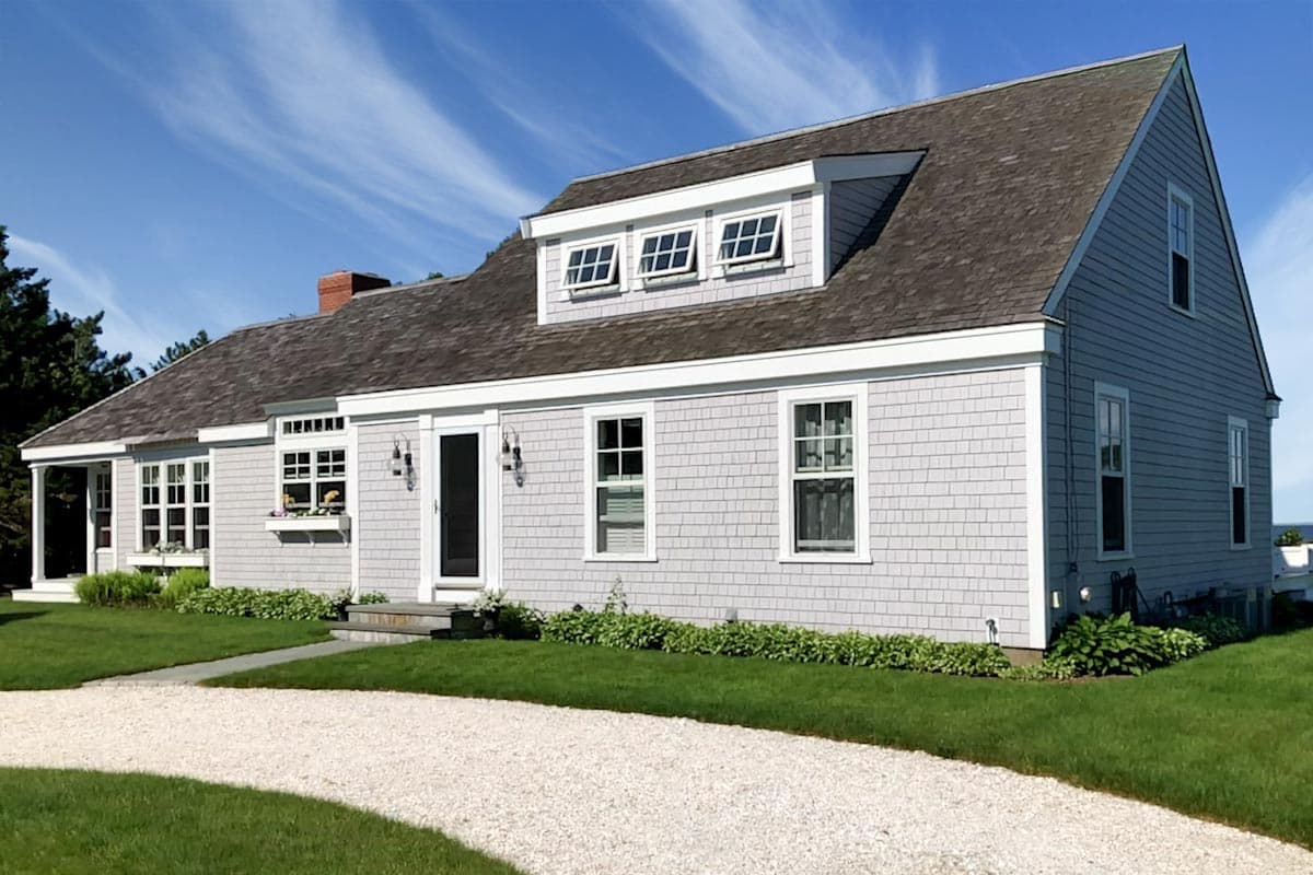 Two-story house plan exterior with shingle siding, dormers, multiple gables, and a covered side porch.