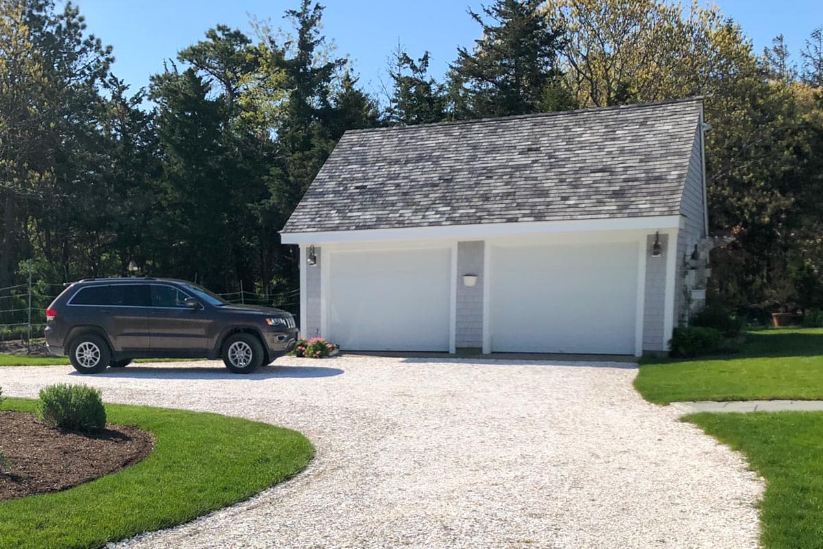 House plan exterior: Two-car garage with asphalt shingle roof, vertical siding, and stone accents.