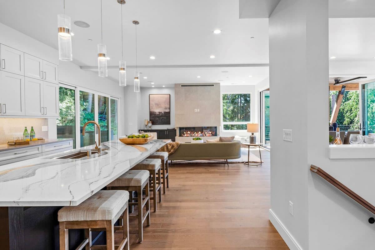 Modern open-plan living area with a large kitchen island, linear fireplace, and ample natural light from expansive windows.
