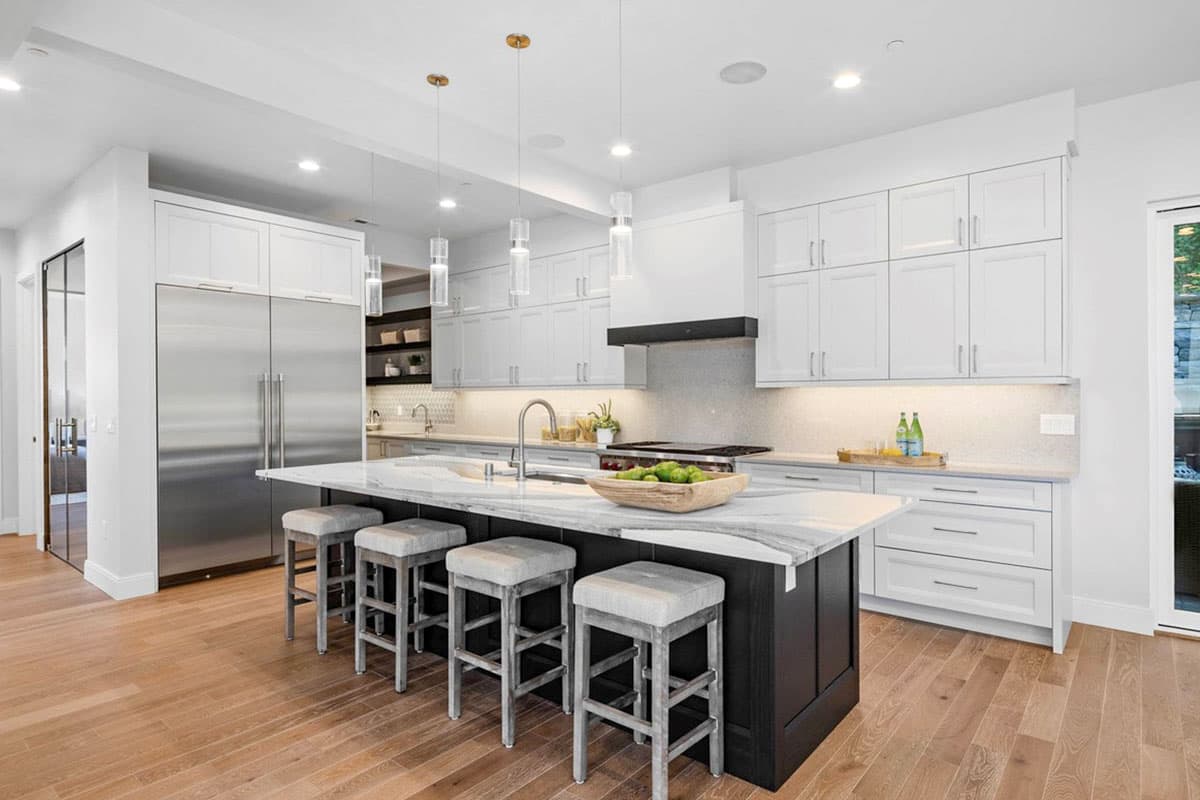 Modern kitchen with island seating, white cabinetry, stainless steel refrigerator, and pendant lighting.