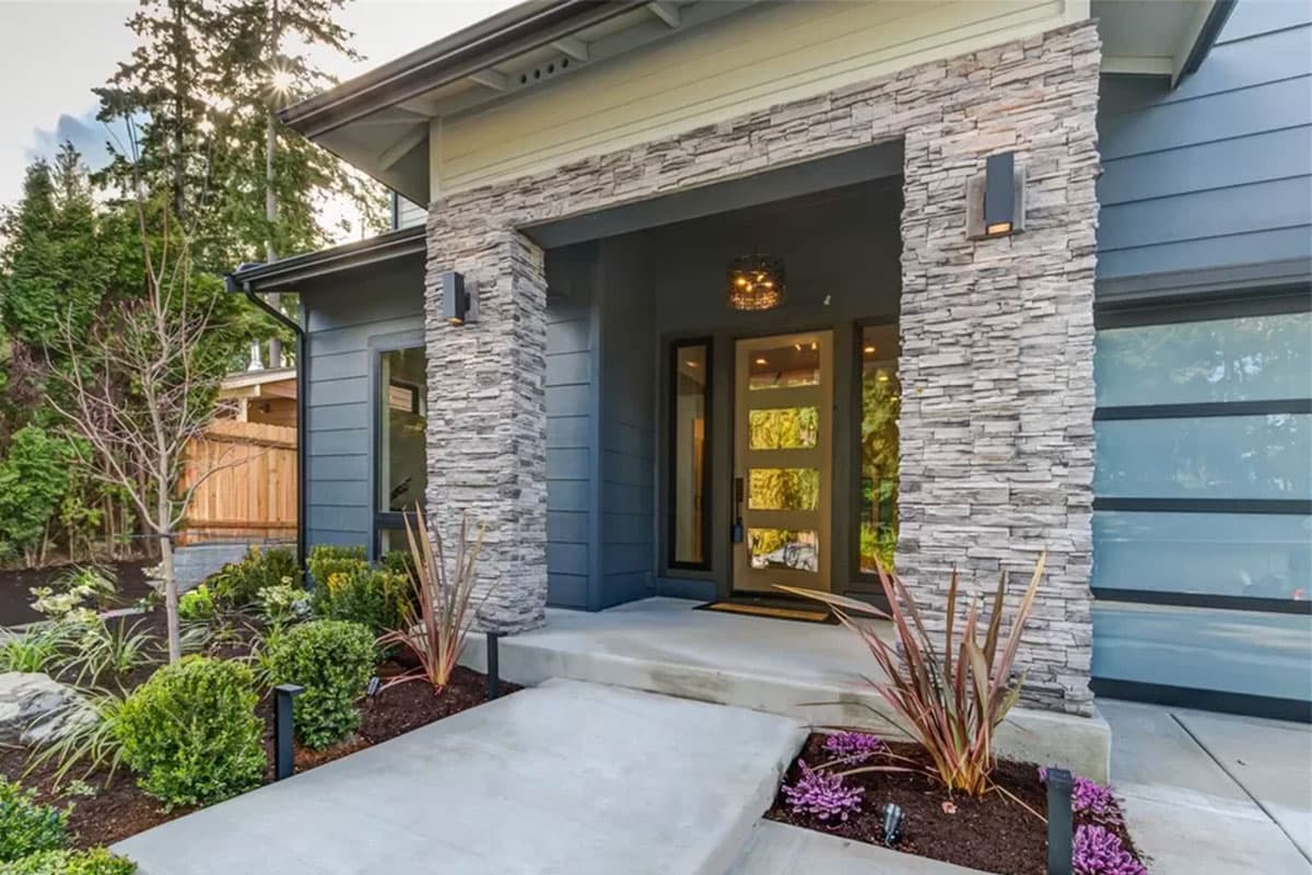 Modern house plan exterior with stone-clad pillars, a glass entry door with wood accents, and a frosted glass garage door.