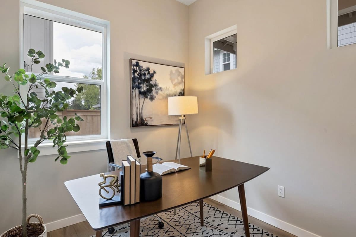 Interior view of a home office with a dark wood desk, black office chair, and abstract wall art.