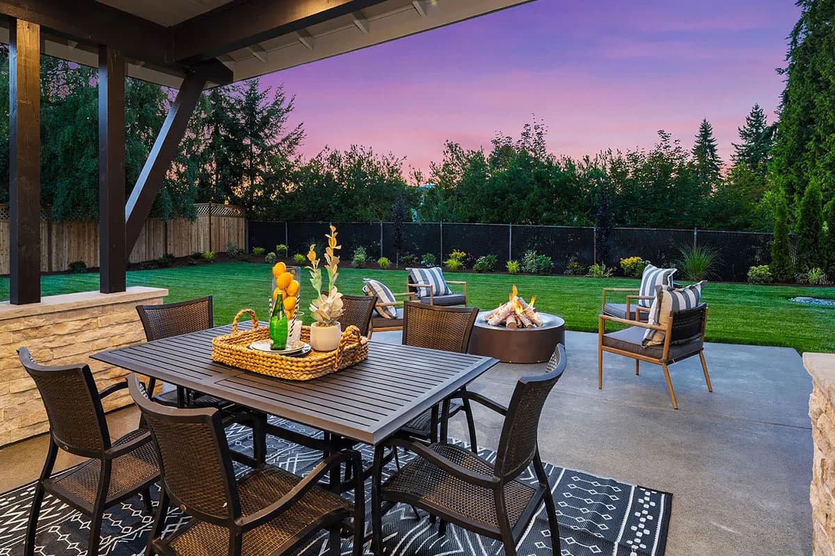Outdoor patio with dining table, fire pit, and seating area under a covered porch with dark wood beams.