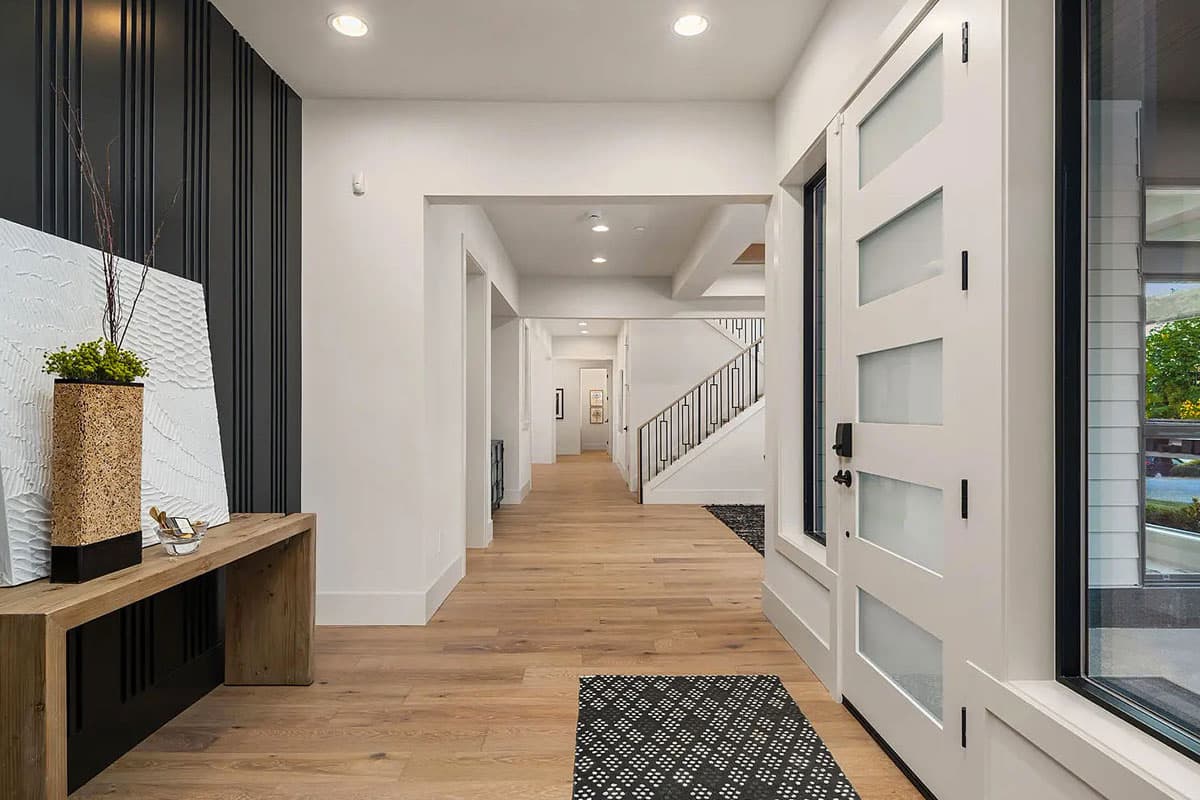 Interior view of a modern entryway with a light wood floor, a geometric-paneled front door, and a contemporary staircase with metal railings.