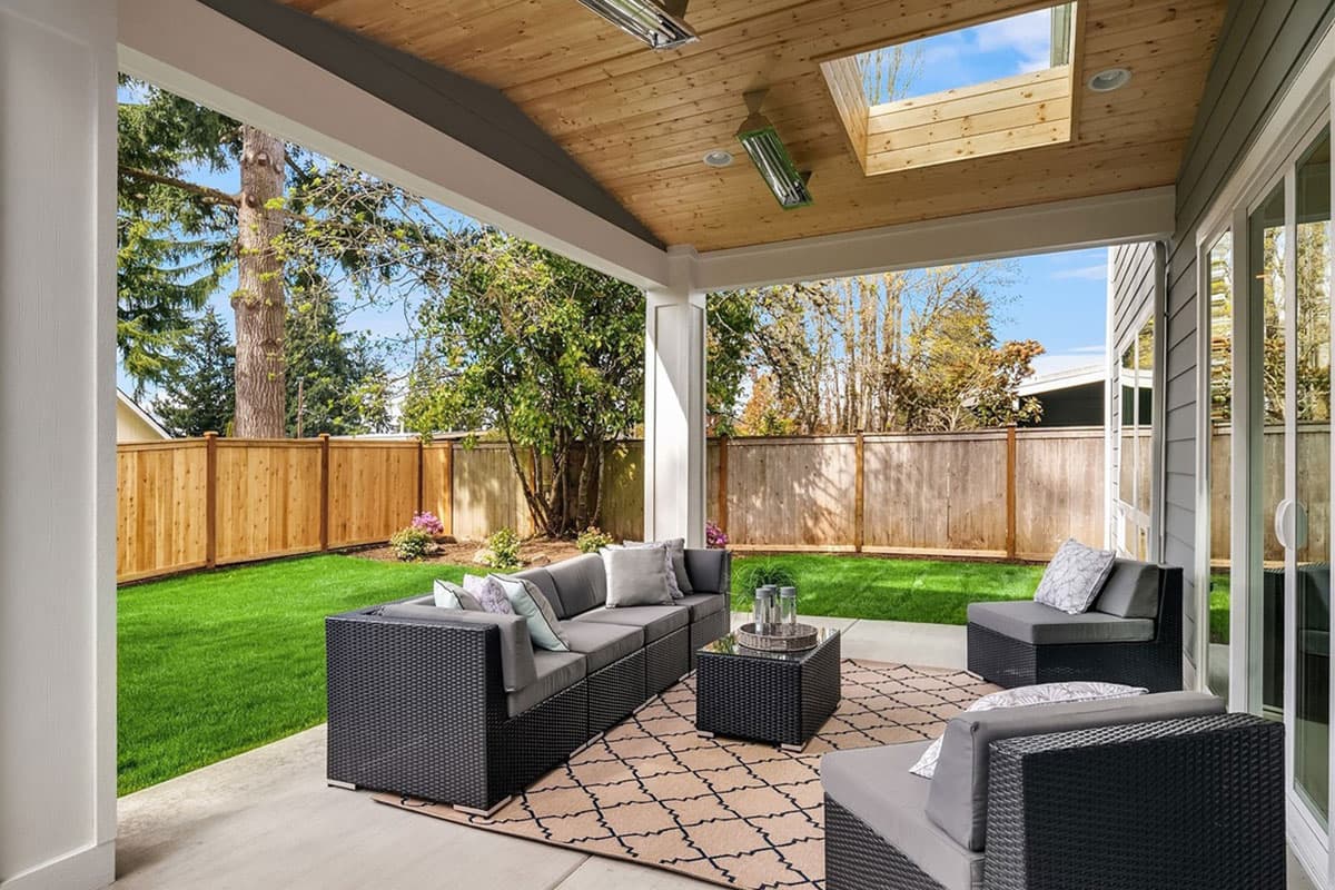 Covered patio with wood ceiling, skylight, and outdoor seating overlooking a fenced backyard with a lawn.