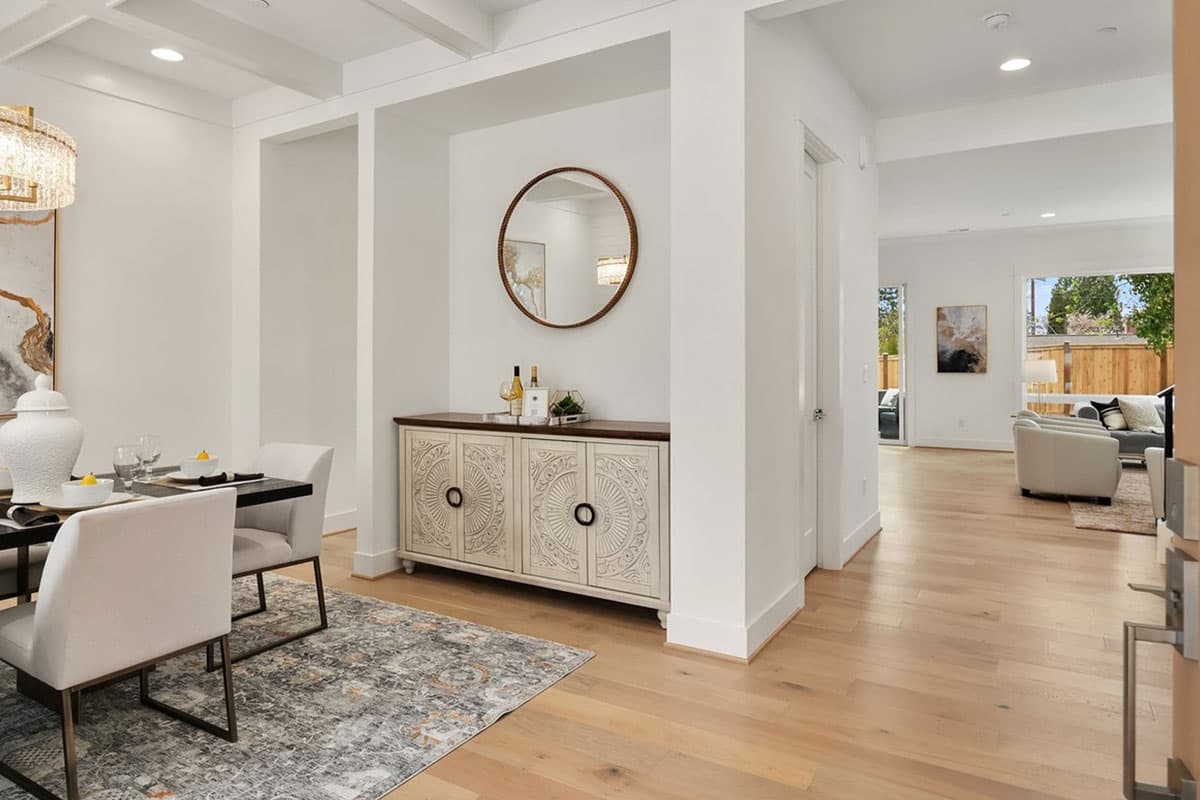 Dining room with coffered ceiling, entryway with console table and mirror, and view into living room with large windows.