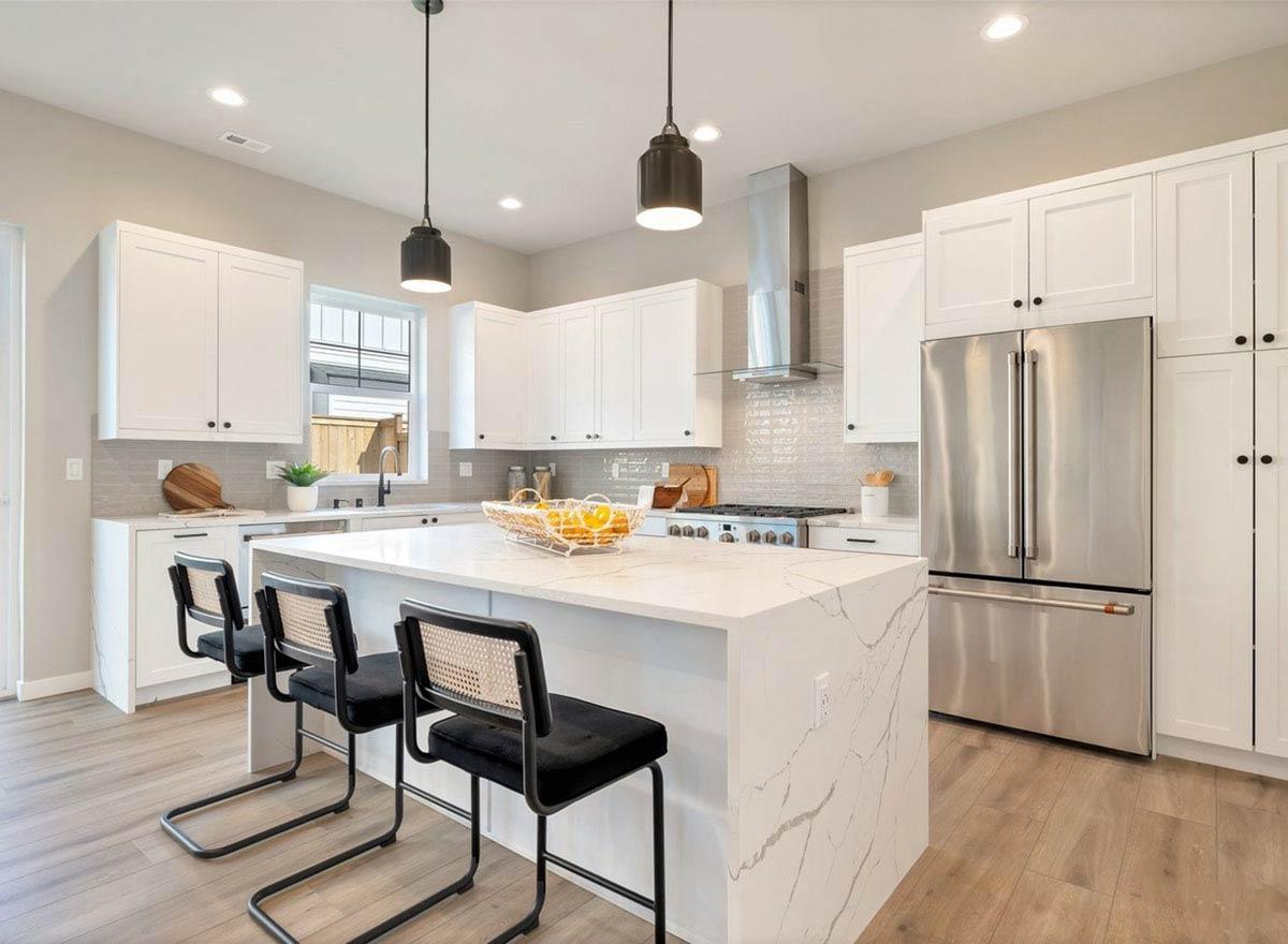 Modern kitchen with white cabinetry, large quartz island with seating, stainless steel appliances, and gas range.