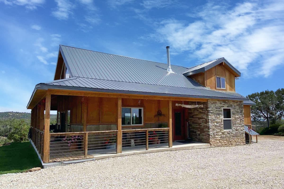 House plan exterior with a wraparound porch, stone foundation, and prominent gabled rooflines.