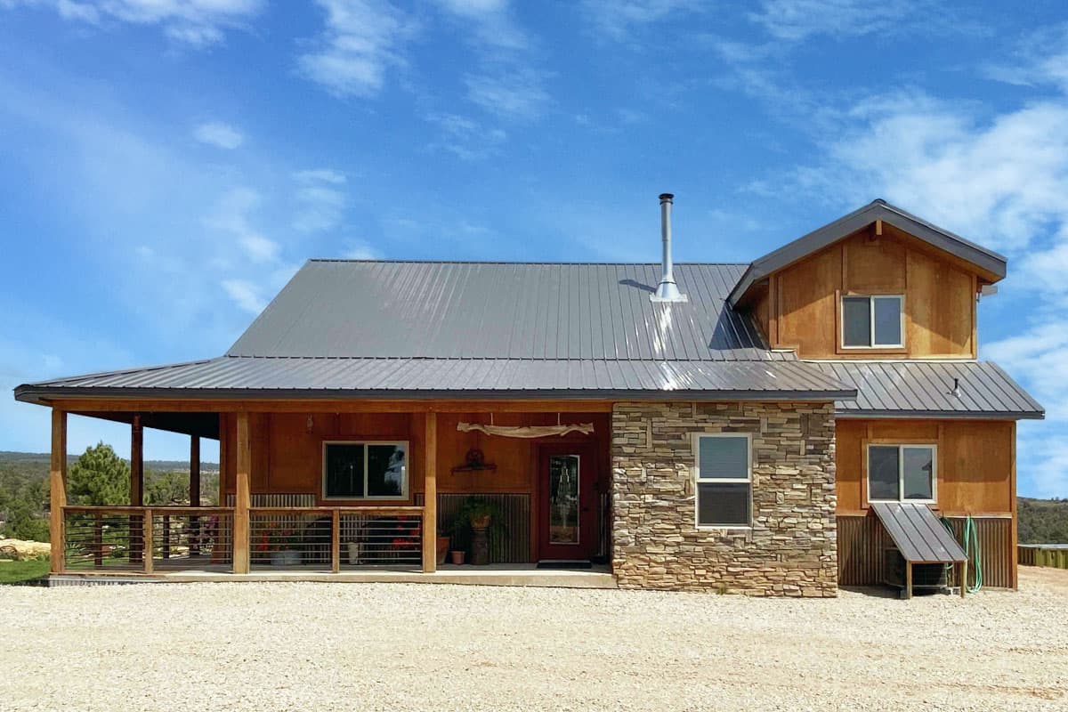 House plan exterior. Two-story, with a metal roof, stacked stone accent wall, and covered porch with exposed support posts.