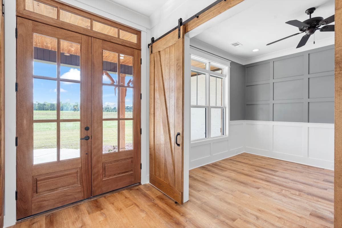 Interior view showing double wood front doors, a wood barn door, and a room with wainscoting and a ceiling fan.