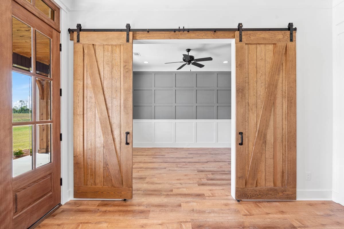Interior view of a room with two large wooden barn doors, a wood floor, and a paneled wall with a ceiling fan.