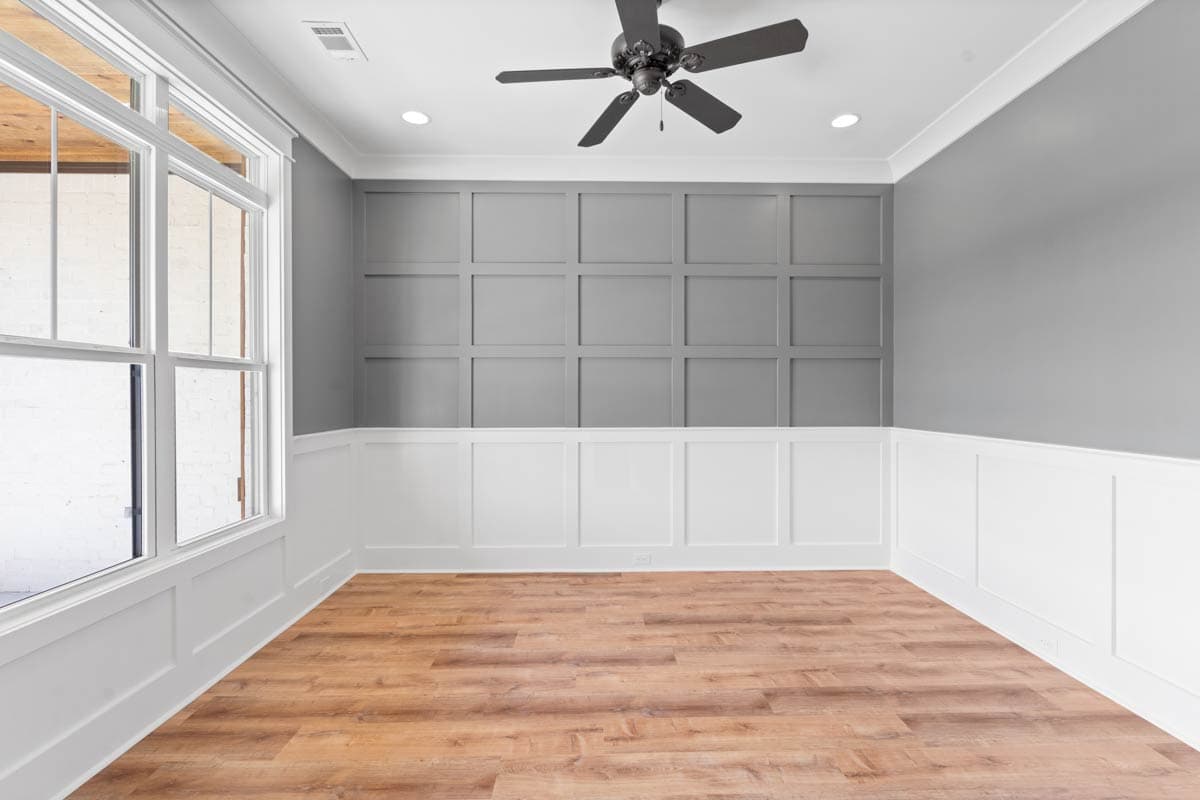 Interior view of room with wainscoting, grid panel accent wall, large window, and ceiling fan.