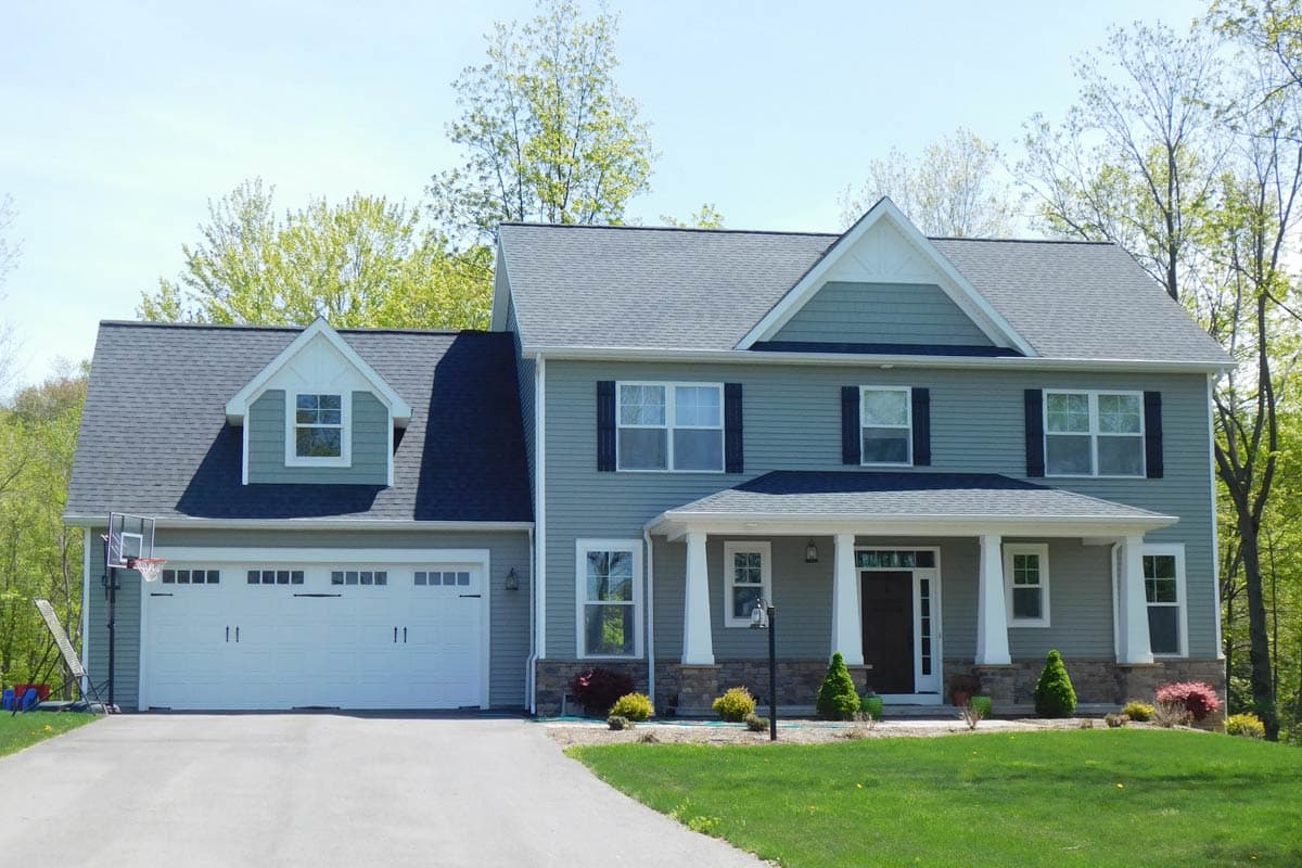 Two-story house plan exterior with a prominent covered front porch, a side-entry garage, and a dormer above the garage.