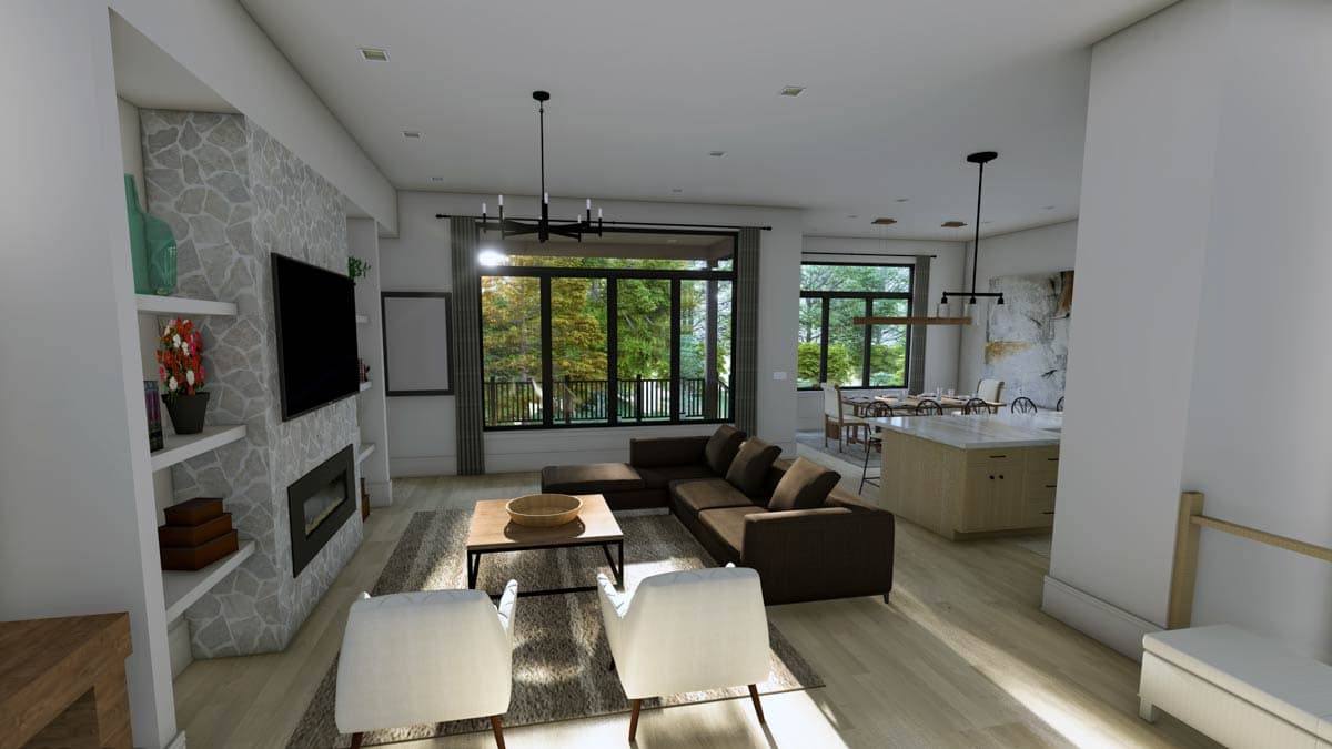 Modern living room with stone fireplace, sectional sofa, island kitchen, and large windows overlooking trees.