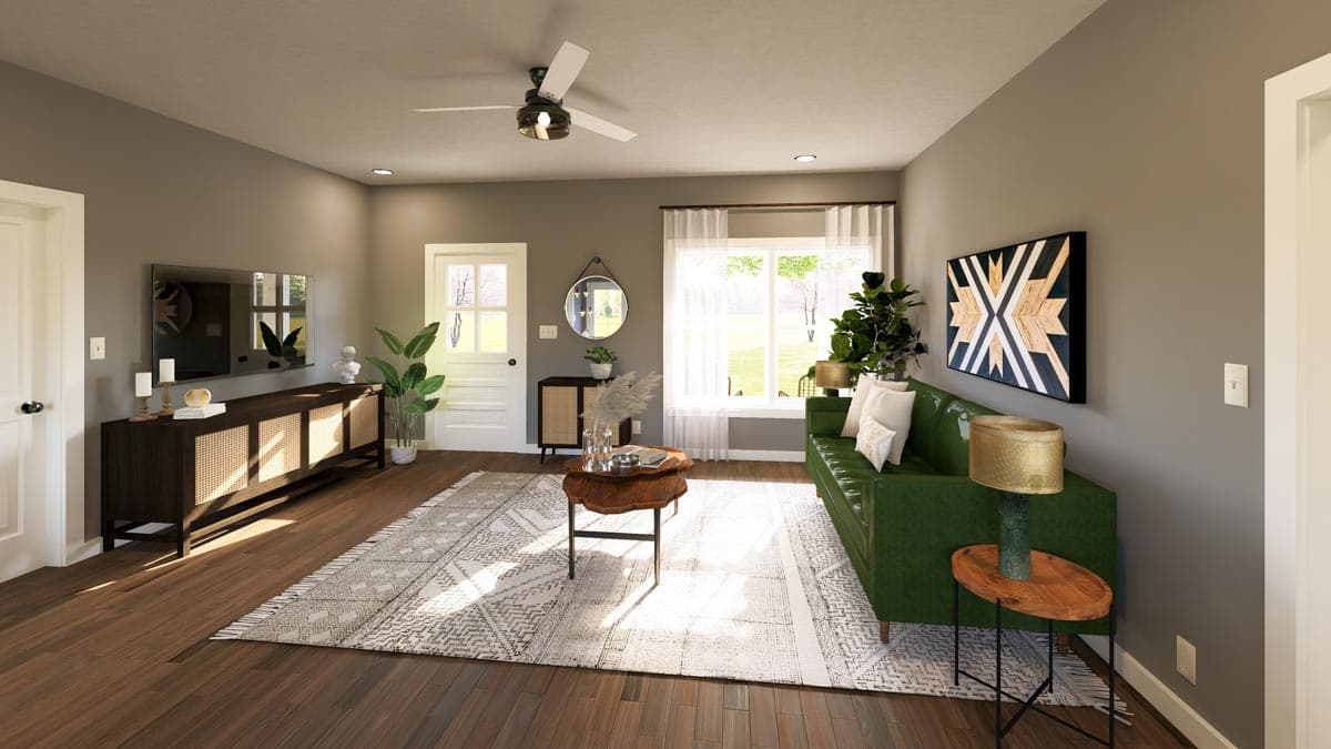 Living room with green sofa, patterned rug, dark wood media console, and large window. A ceiling fan is visible.