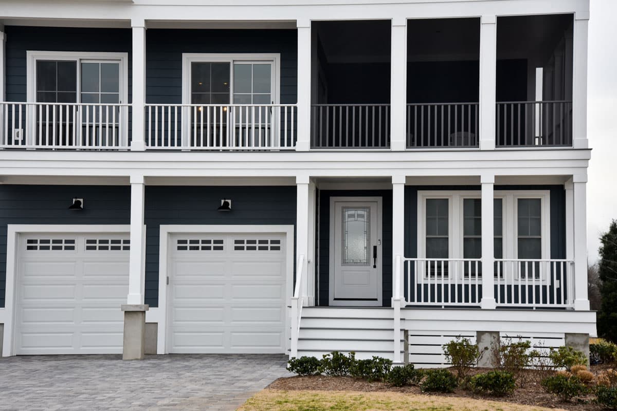 Two-story house plan exterior with white railing balconies, double garage doors, and covered front porch with columns.