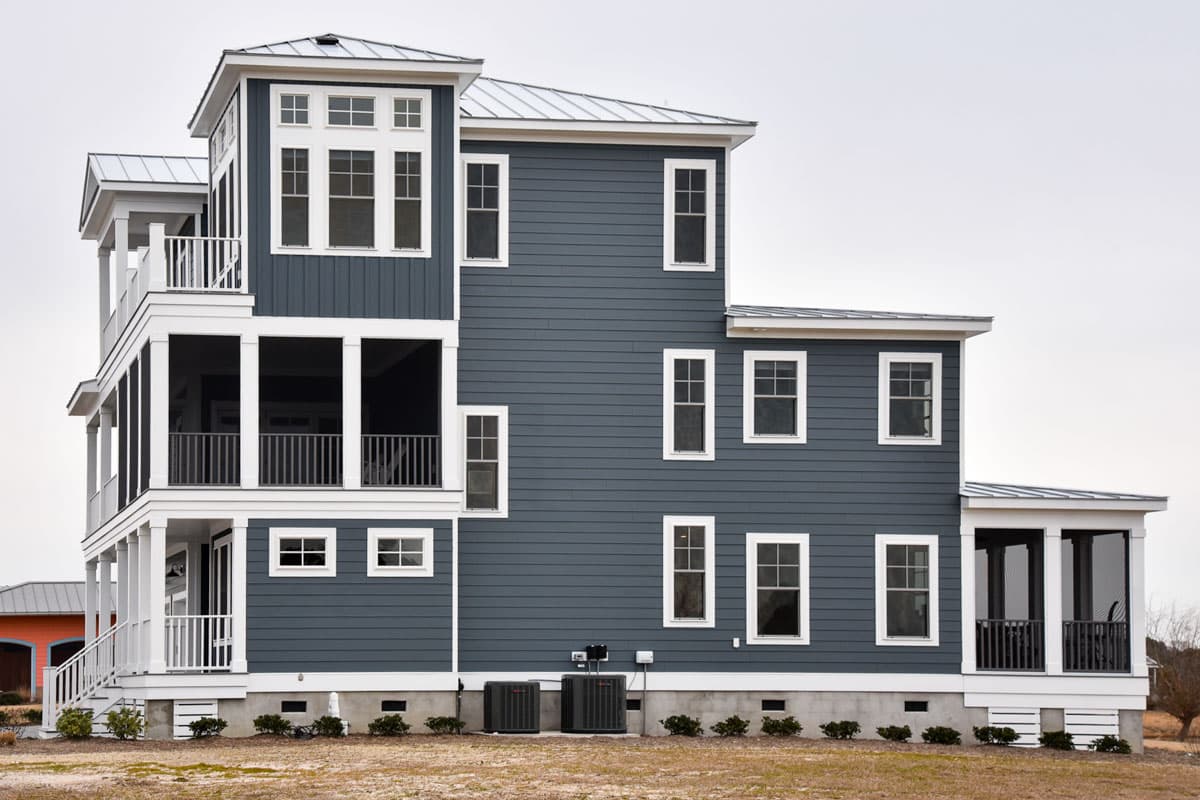 House plan exterior: Modern coastal home with multiple stories, metal roof, screened porches, and numerous windows.