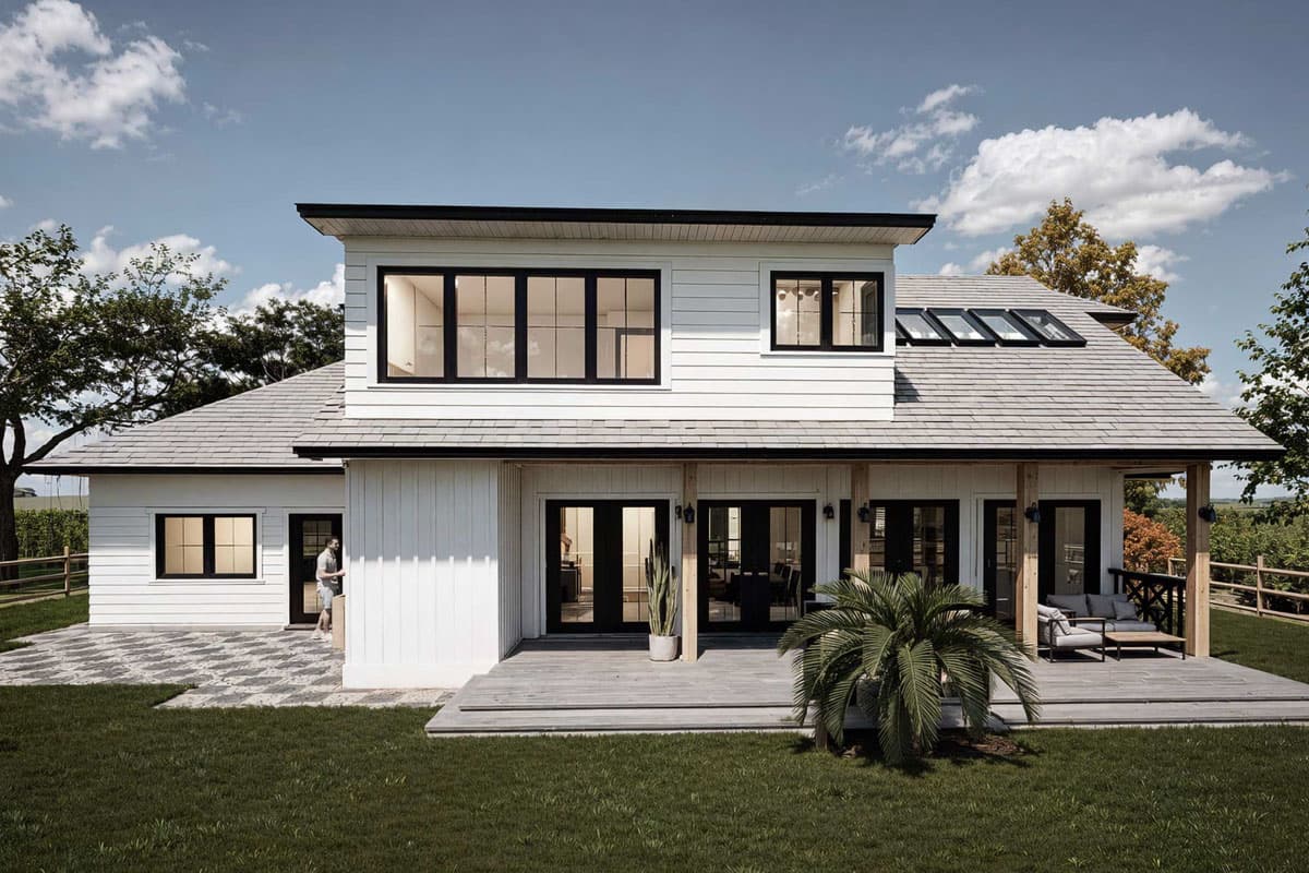 Modern house plan exterior with white siding, a covered deck, multiple gables, and large windows. Two stories visible.