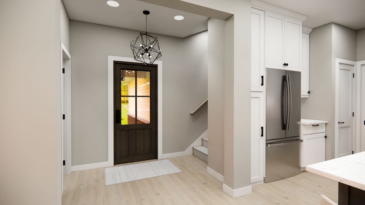Interior view: Entrance foyer with dark wood door, stairs to upper level, and white kitchen cabinets with stainless steel refrigerator.