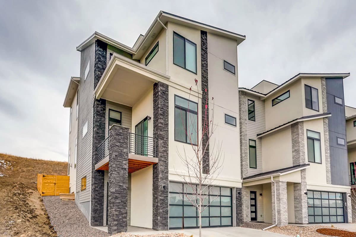 Modern townhouse exterior with stacked stone accents, cantilevered balcony, and multiple garage doors.