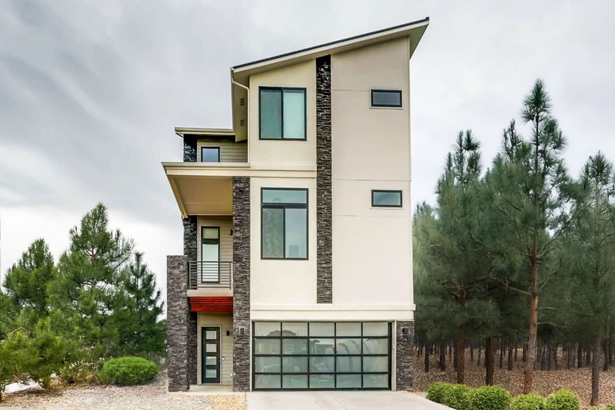 Modern house plan exterior. Three-story home with a flat roof, large windows, and a glass-paneled garage door. Stone accent columns are visible.